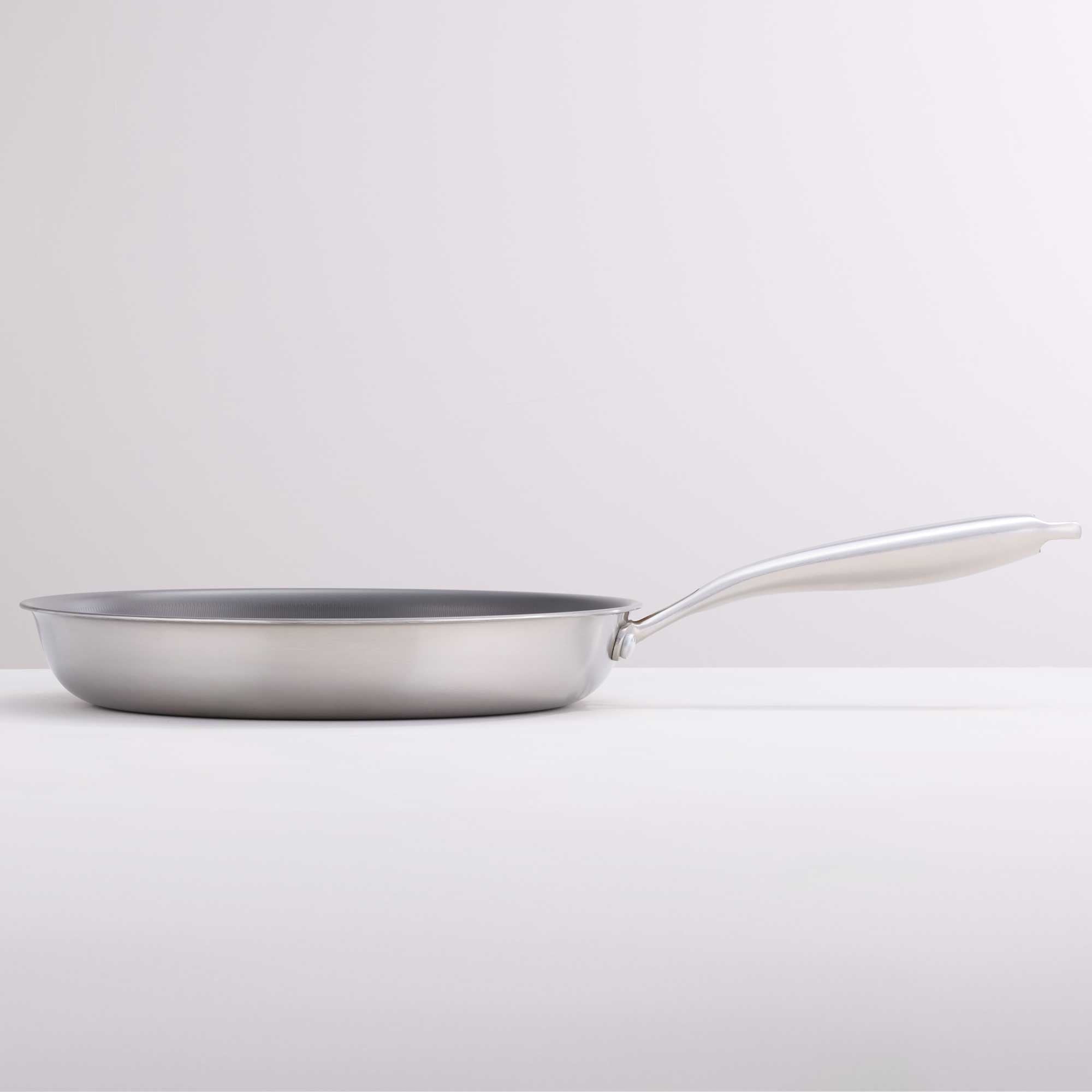 A stainless steel frying pan with a long, curved white handle, photographed on a clean white studio background.
