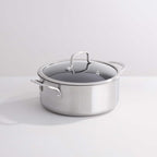 A stainless steel casserole with a glass lid and metal handles, photographed on a clean white studio background.