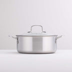 A stainless steel casserole with a glass lid and side handles, photographed on a clean white surface against a light gray background.