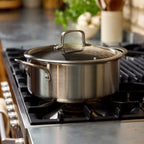 A stainless steel casserole with a glass lid sits on a gas stovetop in a kitchen setting.