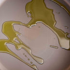 A close-up of olive oil drizzled in a zigzag pattern across the bottom of a light beige textured pan.
