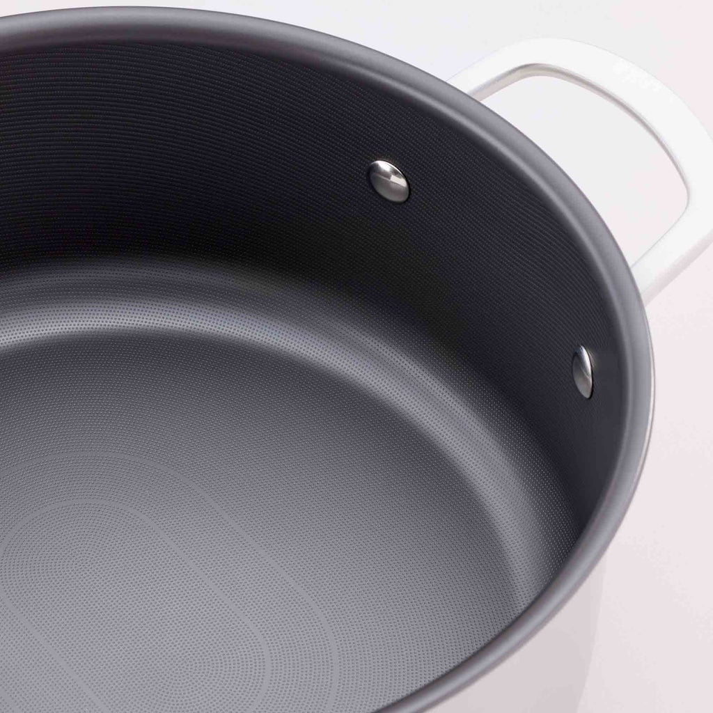 Close-up of a silver saucepan with a dark gray non-stick interior, showing the textured coating and a silver rivet near the rim.
