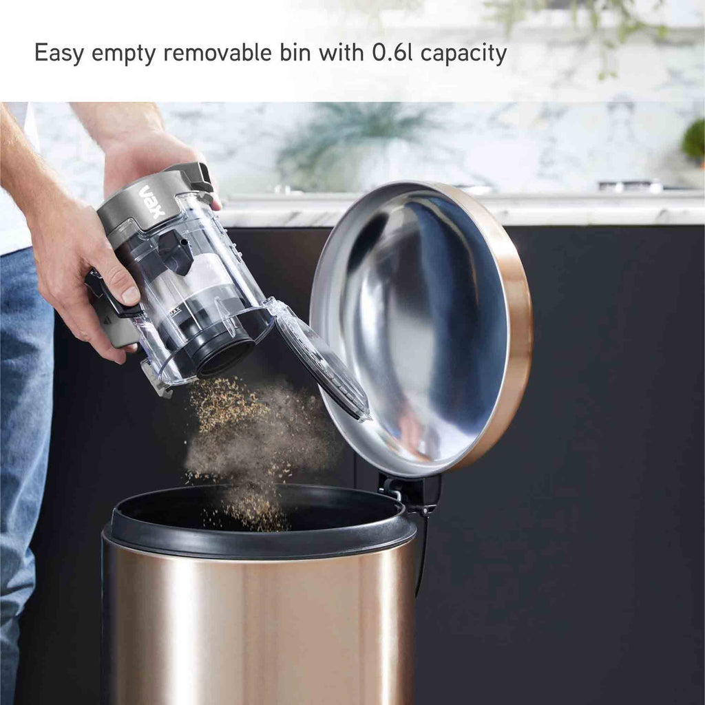 A person empties a clear and gray handheld vacuum into a brushed stainless steel trash can with the lid open. Text at the top reads 'Easy empty removable bin with 0.