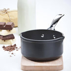 Black milk pan on a wooden stand with chocolate bars and a bottle in the background