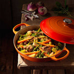 Volcanic Le Creuset casserole dish with a lid filled with vegetable stew on a wooden surface.